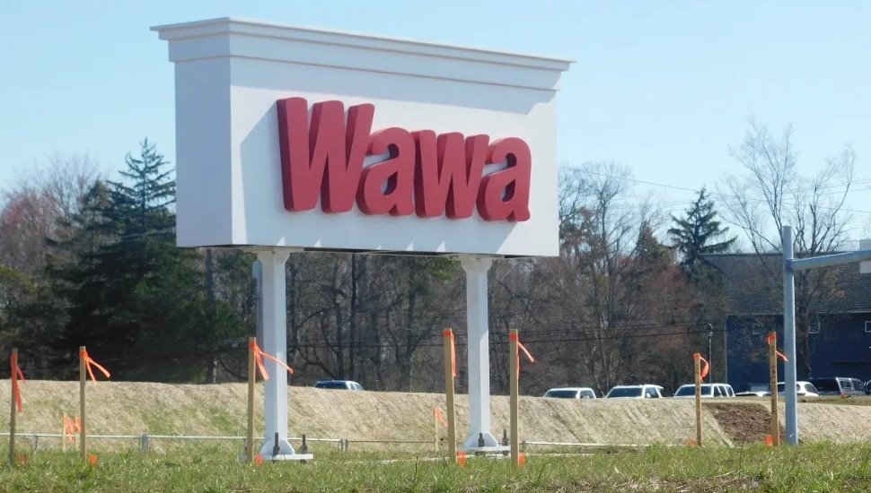 A free-standing Wawa sign in a parking lot with a field in the background.