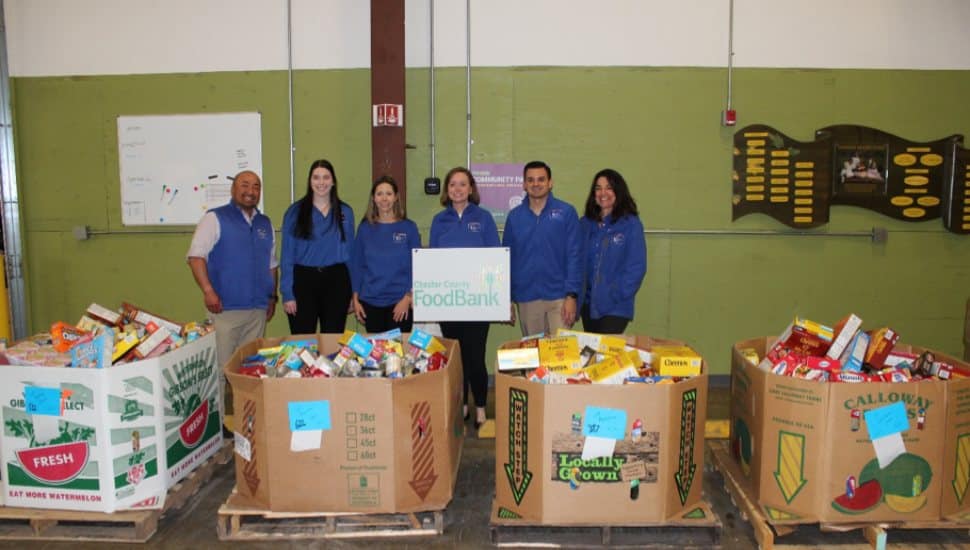 First Resource Bank team members pose with large boxes of donated food at Chester County Food Bank, celebrating their victory in a community food drive competition.