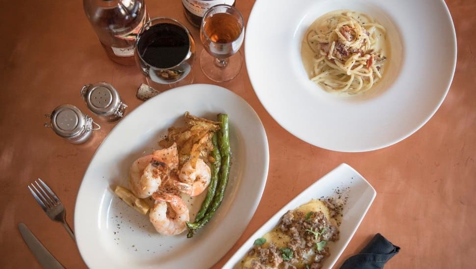 A shirmp dish, a pasta dish and a third entree in plates sitting on a table with spice shakers nearby.