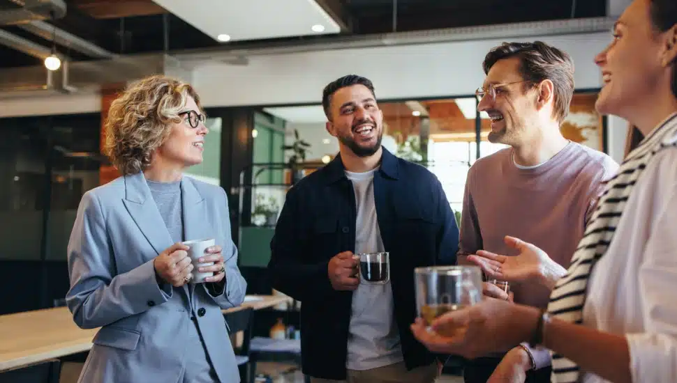 Two men and two women have a conversation while holding cups of coffee.