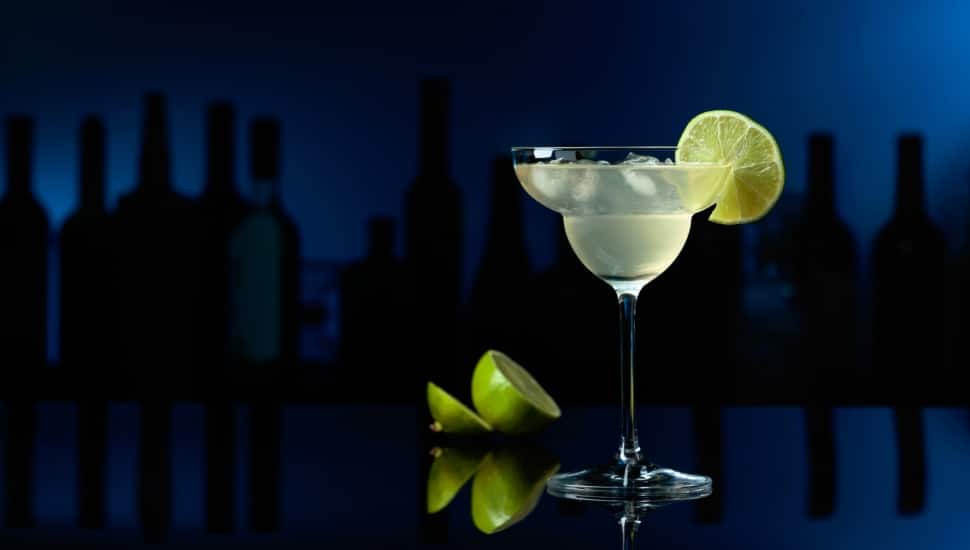 A Cocktail Margarita on a black reflective background, with a lime on the table.