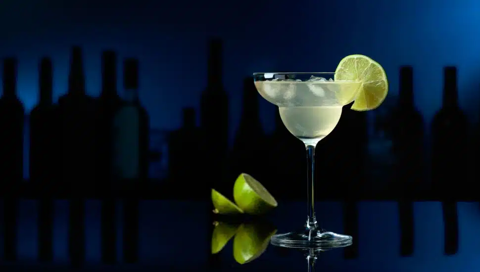 A Cocktail Margarita on a black reflective background, with a lime on the table.