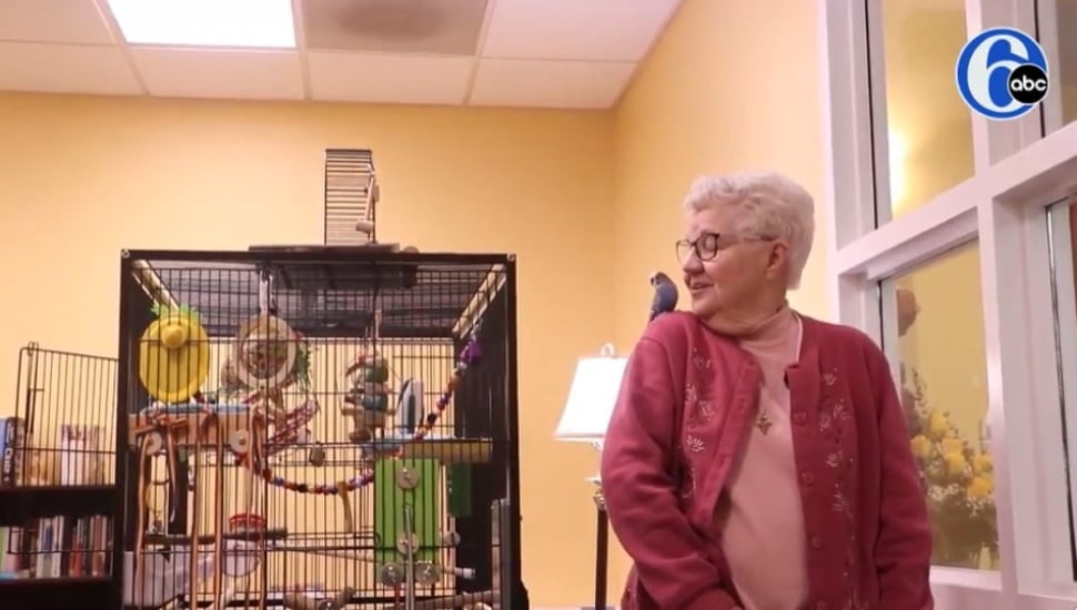 Sister Stephanie Marie Unger talks with a parakeet named Francis sitting on her shoulder with a bird cage nearby.