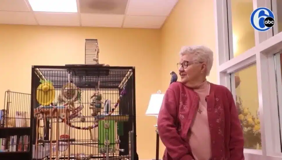 Sister Stephanie Marie Unger talks with a parakeet named Francis sitting on her shoulder with a bird cage nearby.