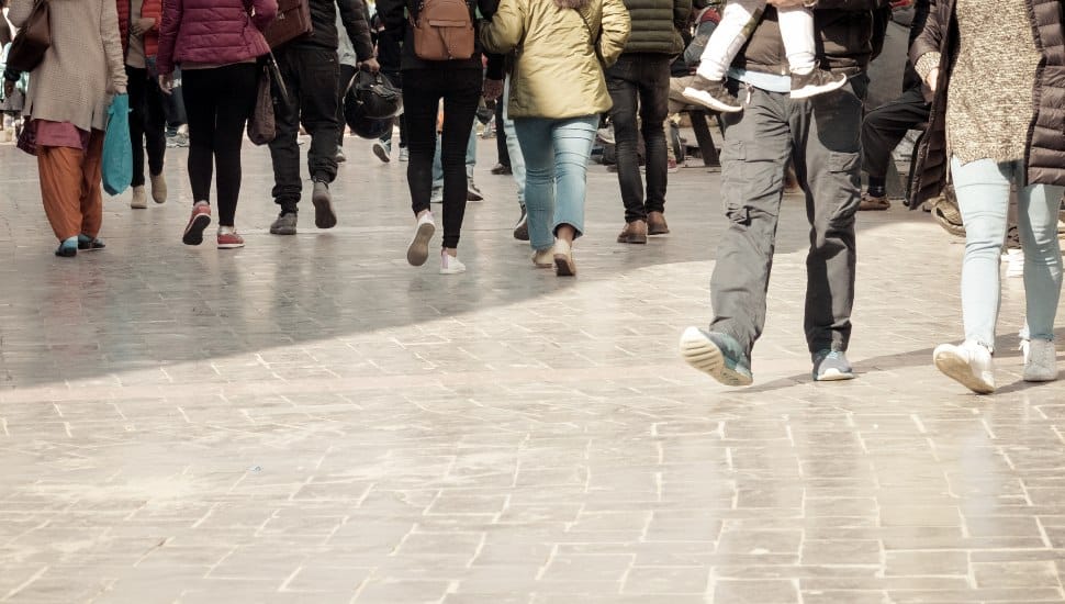 A large group of people walking on a marble floor, seen only from the waist down.
