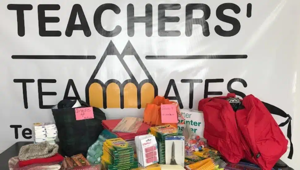 A table filled with school supplies for students, with a Teachers' Teammates poster on the wall behind it.