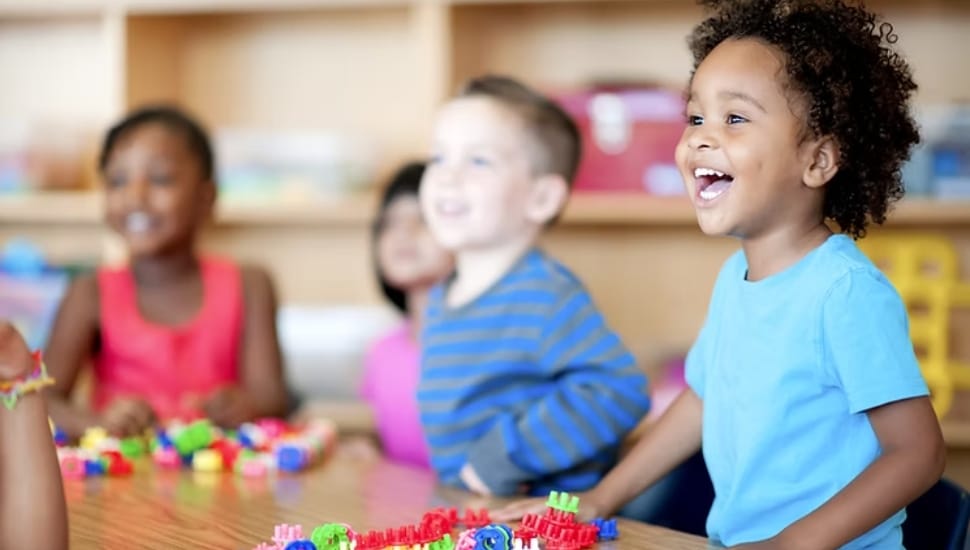 Three children playing at a table looking at something and laughing.