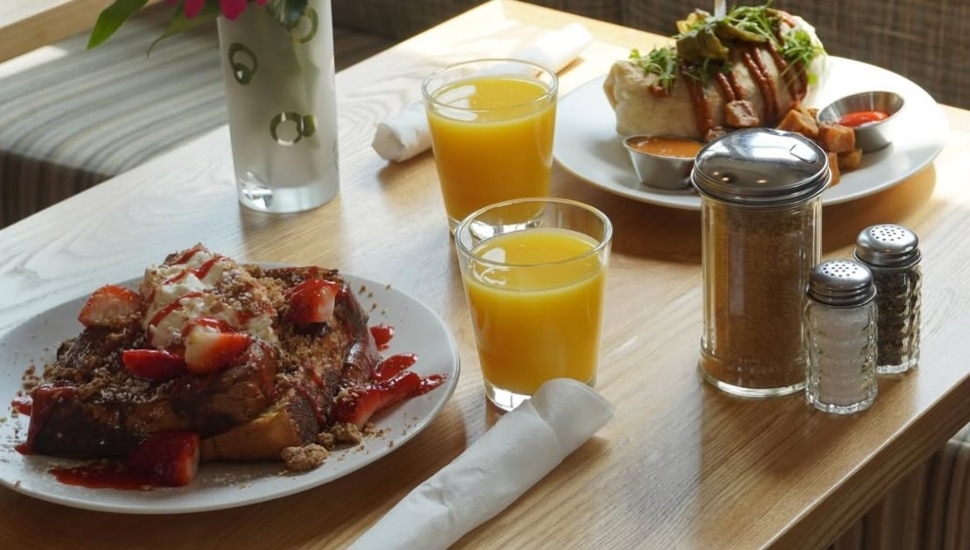A table laid out with two plates loaded with brunch entrees, orange juice and more from Cafe Lift.