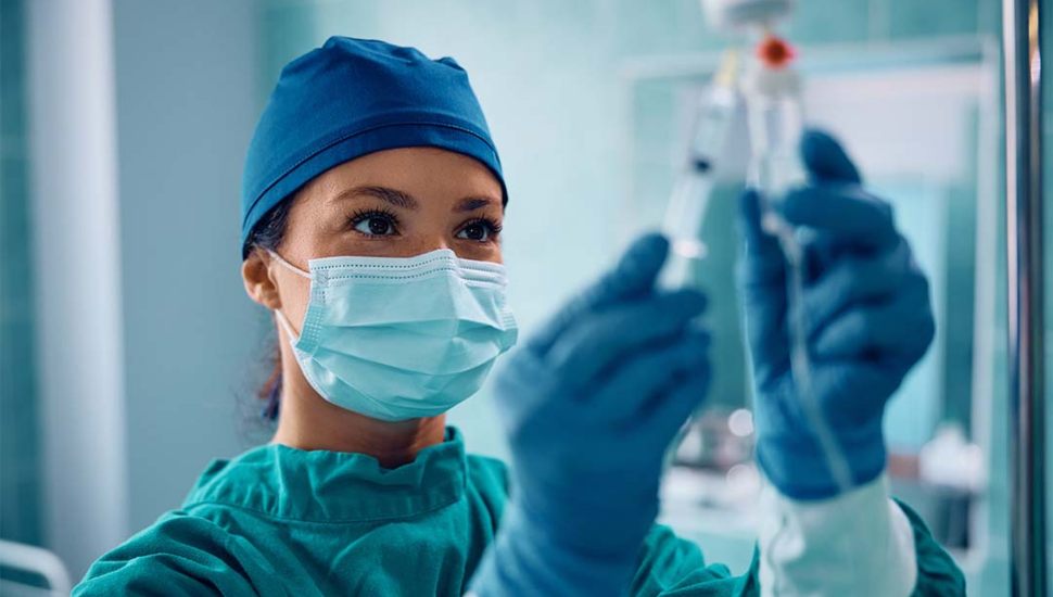 A close up of a nurse wearing scrubs and a mask loading up an IV.