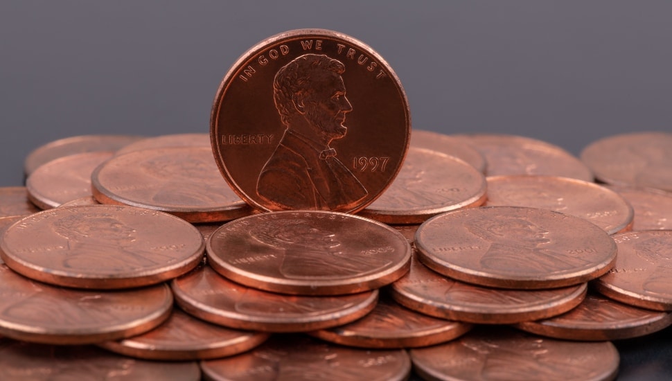 A penny stands on end amongst a pile of pennies.