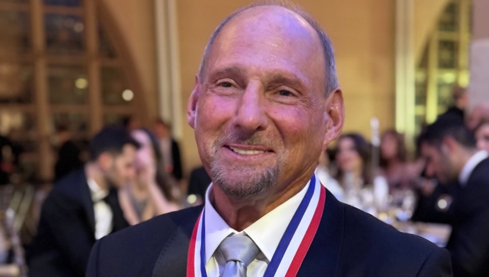 Older banking executive smiles in dark suit and white shirt with award medal.