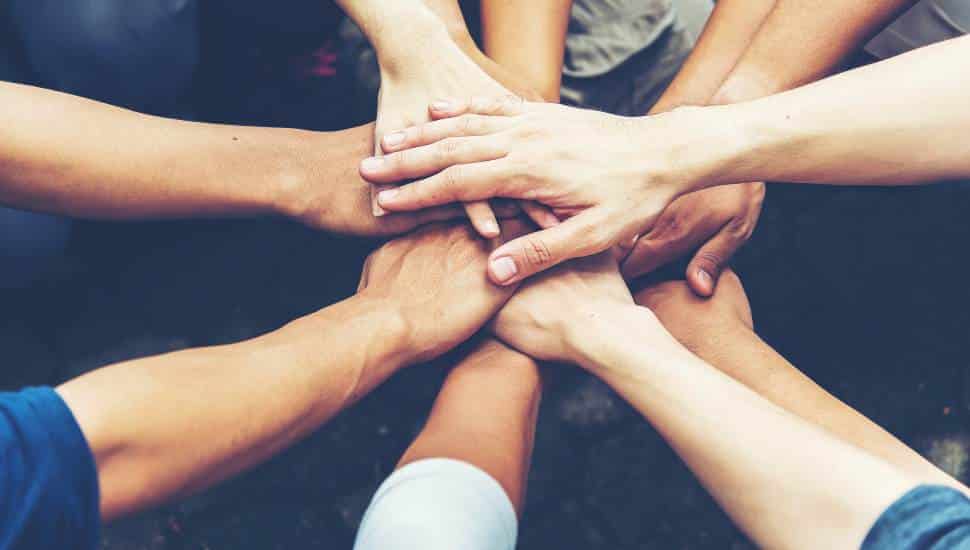 A diverse group of people standing outdoors with their hands stacked together in a show of unity and teamwork, symbolizing solidarity, cooperation, and shared purpose.