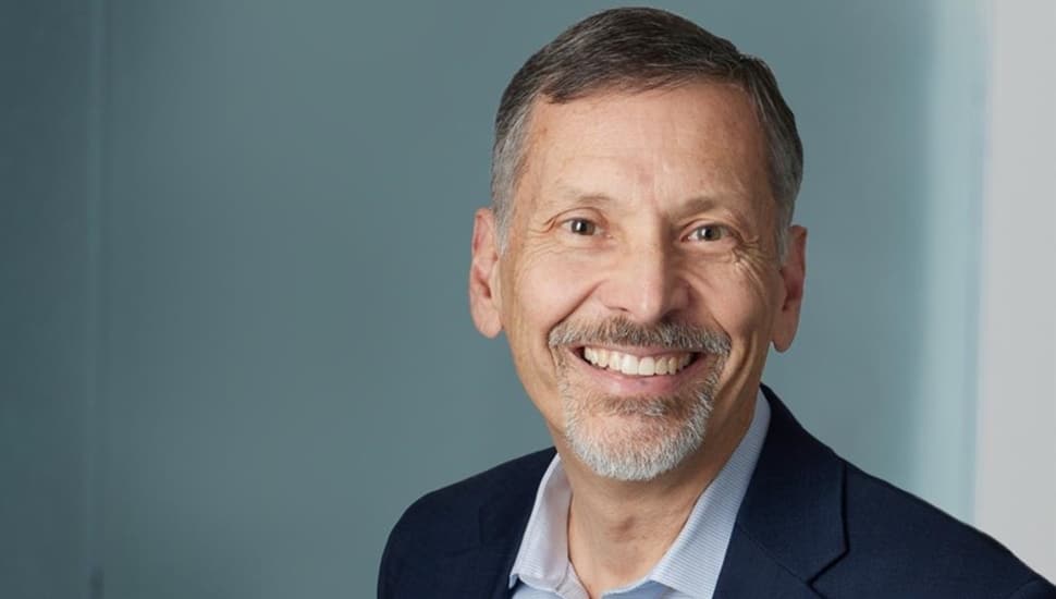 Headshot of older male business executive in dark blue suit and open collared shirt.