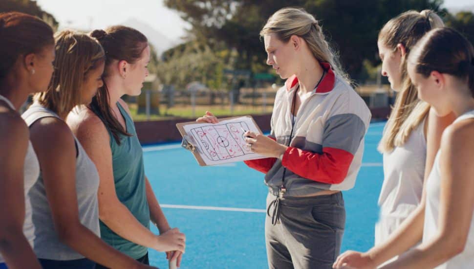 A female coach reviews a play with four teen girl student athletes.