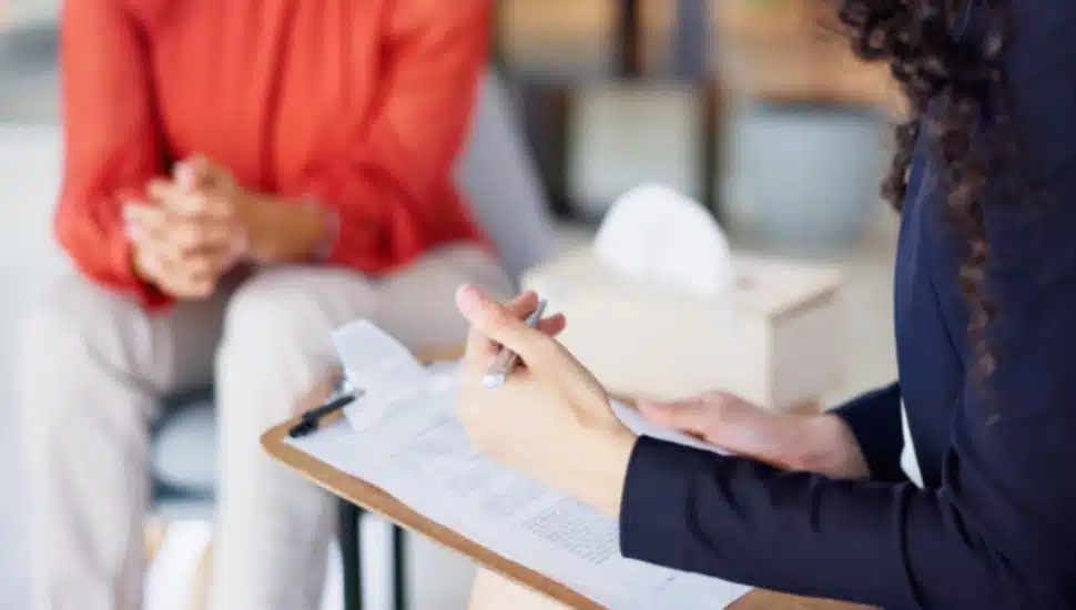 A worried person with hands clasped gets help from a worker.