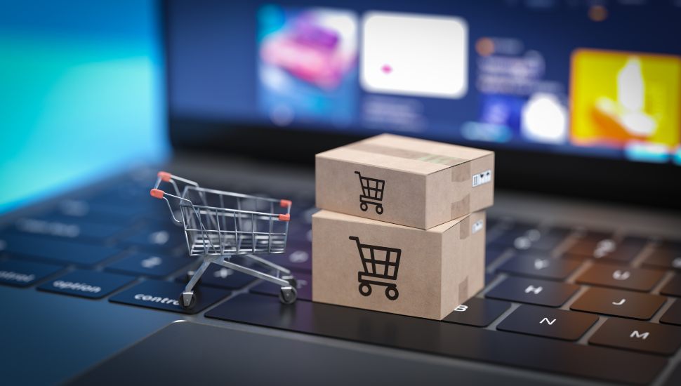 Blocks with shopping cart images sit on top of a laptop keyboard with online shopping logos on the screen.