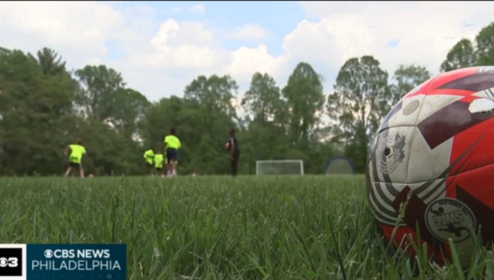 A soccer ball is in the foreground on an outdoor grass soccer field as Benchmark School students participate in soccer practice.