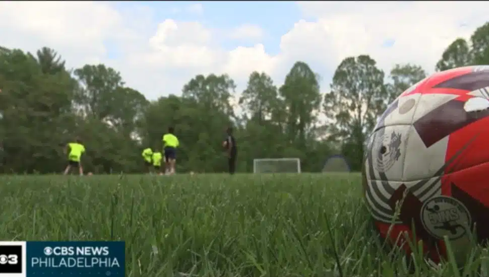 A soccer ball is in the foreground on an outdoor grass soccer field as Benchmark School students participate in soccer practice.
