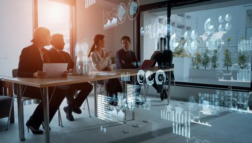 A team of five employees are sitting at a table with laptops, with computer images superimposed.