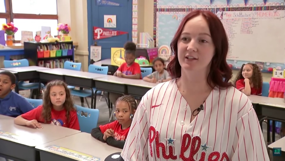 Teacher Amber Kiley with her elementary school students behind her sitting at desks.