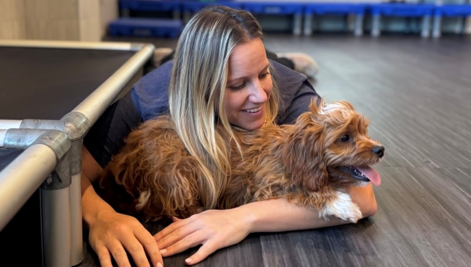 Blond woman hugs her dog while lying on the floor.