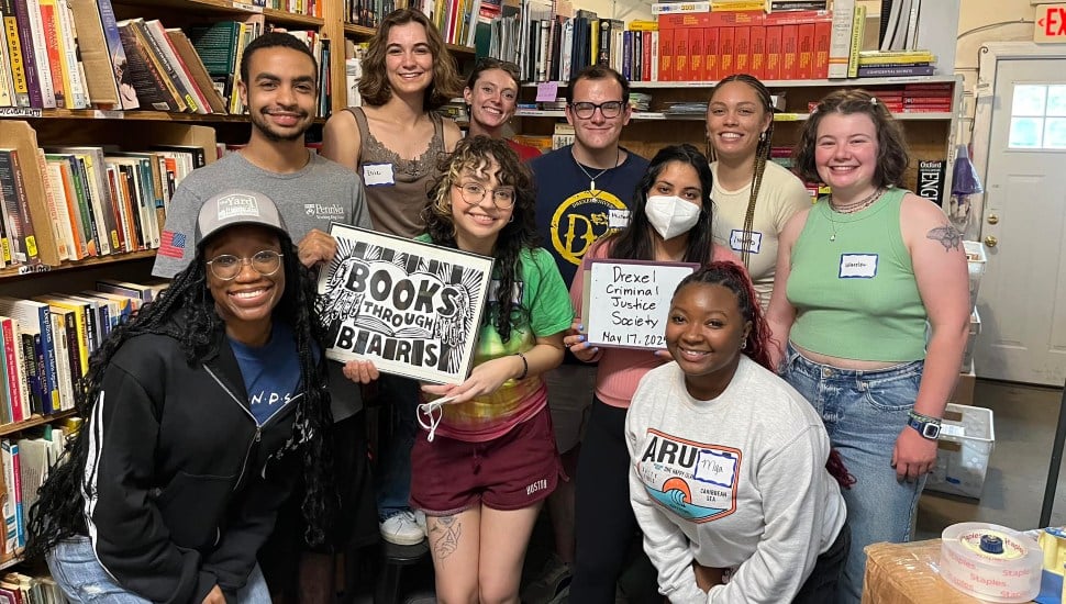 Members of Books Through Bar gather together in a book store or library holding some books.
