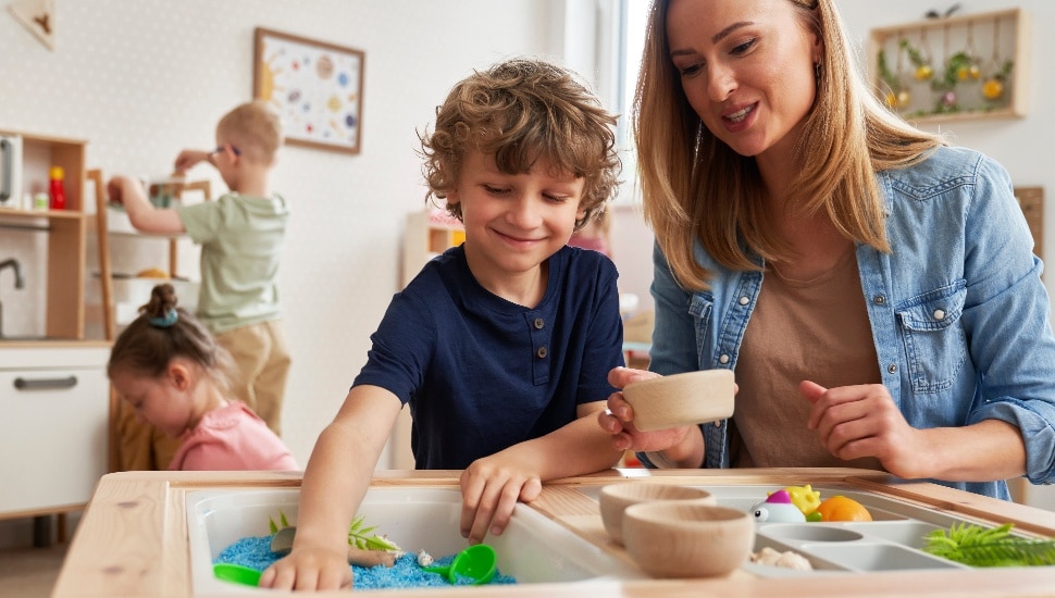 A child care provider works on a project with a young boy.