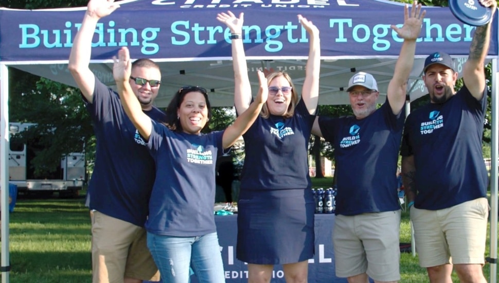 Bank employees in blue shirts lift their arms in celebration.