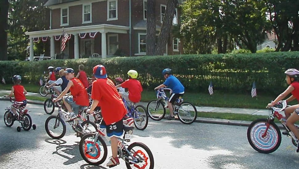 Kids on bicycles ride down a shaded suburban street.
