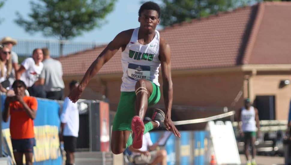 Donte Dockery, wearing a Wilmington University track uniform, is mid-air during his triple jump at the 2025 NCAA Division II Outdoor Track and Field Championships. He appears focused and powerful, with fans and competitors watching from the background.