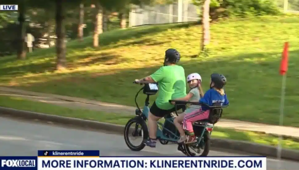 A mom rides an E-bike down the street with her two children.
