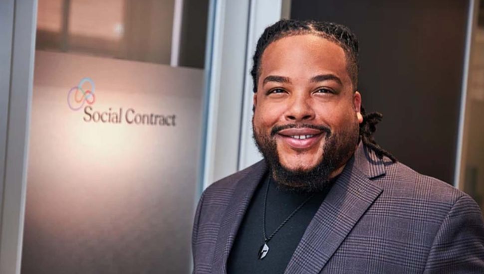 Ron Berry, CEO of Social Contract, smiling in front of the company logo at their office.
