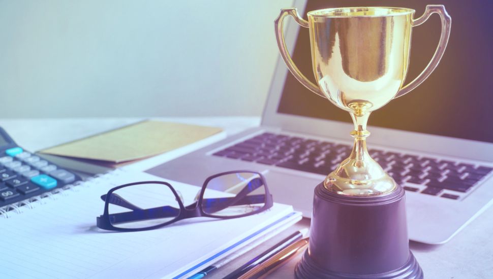 Trophy decoration on working table, achieve concept. There are glasses, chart paper and a laptop in the background.