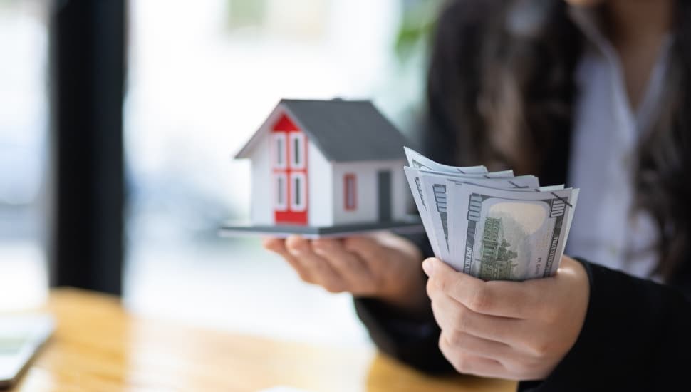 A man holds cash in one hand a model house in another.