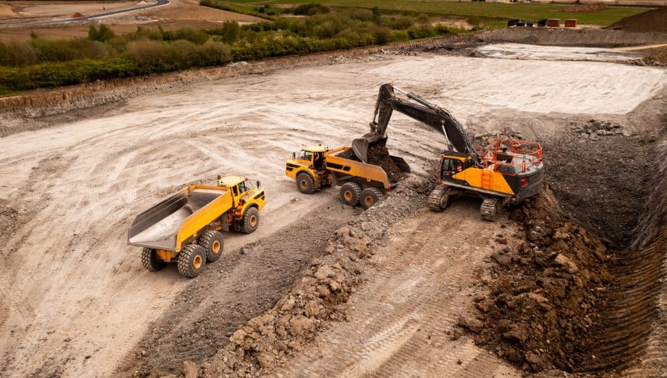 Aerial view of a crane and truck moving earth and soil on a brownfield site.
