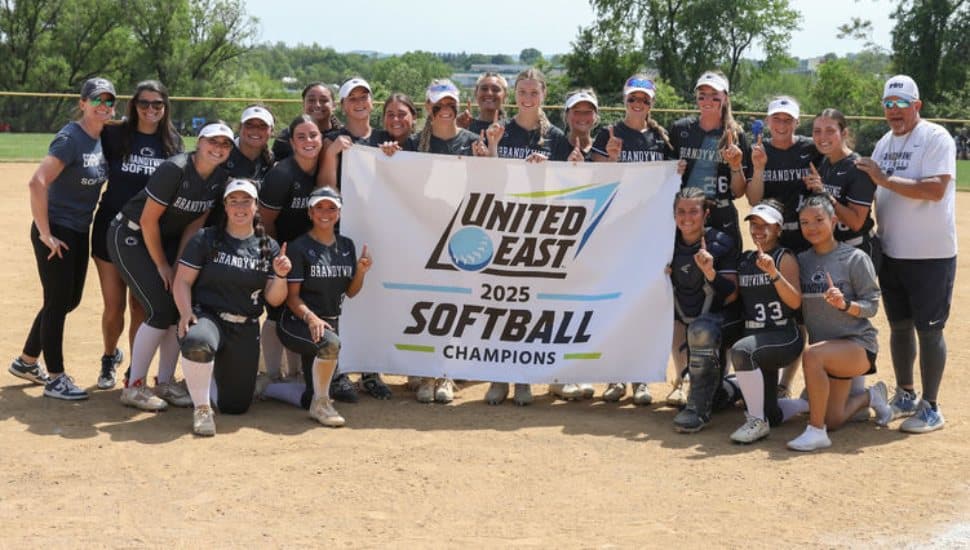 Penn State Brandywine's softball team holds the championship banner on the softball field.