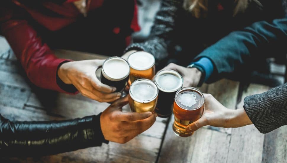 Hands holding mugs of beer toast each other.