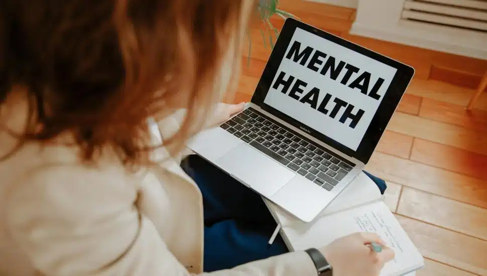 Woman looks at laptop computer with the words Mental Health on the screen.