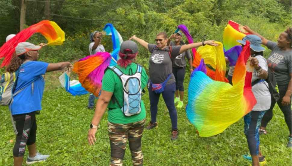 Middle-aged women twirl rainbow-colored sheets in the woods.
