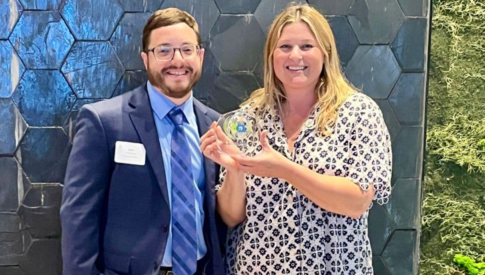 Two Essential Utilities representatives smiling and holding a Civic 50 Greater Philadelphia award in front of a decorative wall.