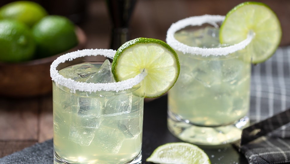 Two salt-rimmed margaritas in a glass with a lime slice.