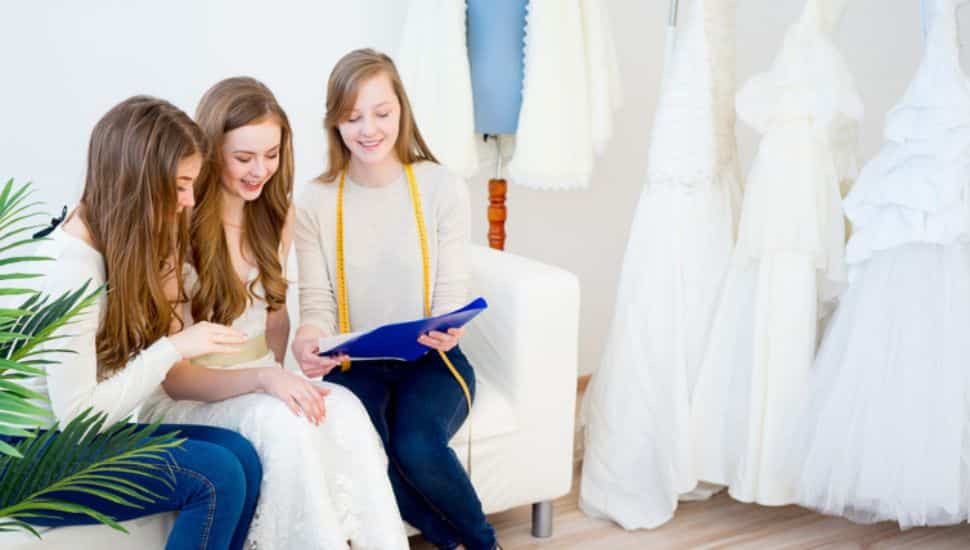 Three seated women in a bridal dress shop look at a planner.
