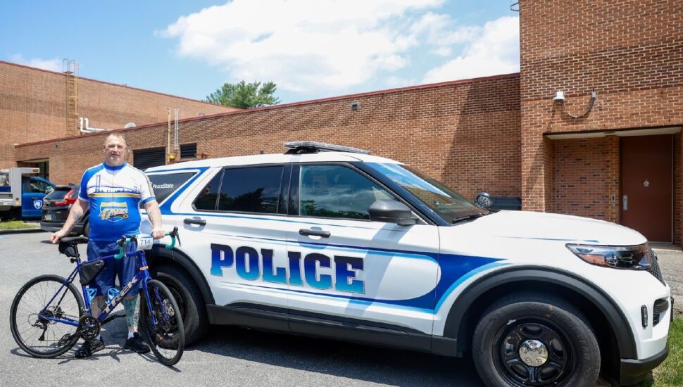 Bill Carter, a Penn State Brandywine University Police and Public Safety Officer poses with his bike in front of a police car.