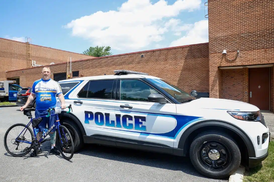 Bill Carter, a Penn State Brandywine University Police and Public Safety Officer poses with his bike in front of a police car.