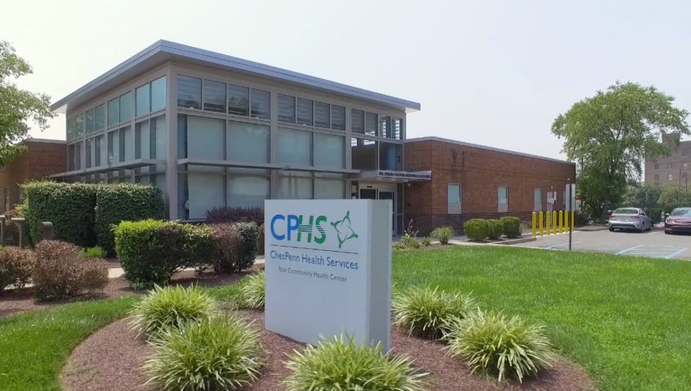 Exterior view of ChesPenn Health Services building with modern glass and brick architecture, landscaped greenery, and a sign reading "ChesPenn Health Services – Your Community Health Center.
