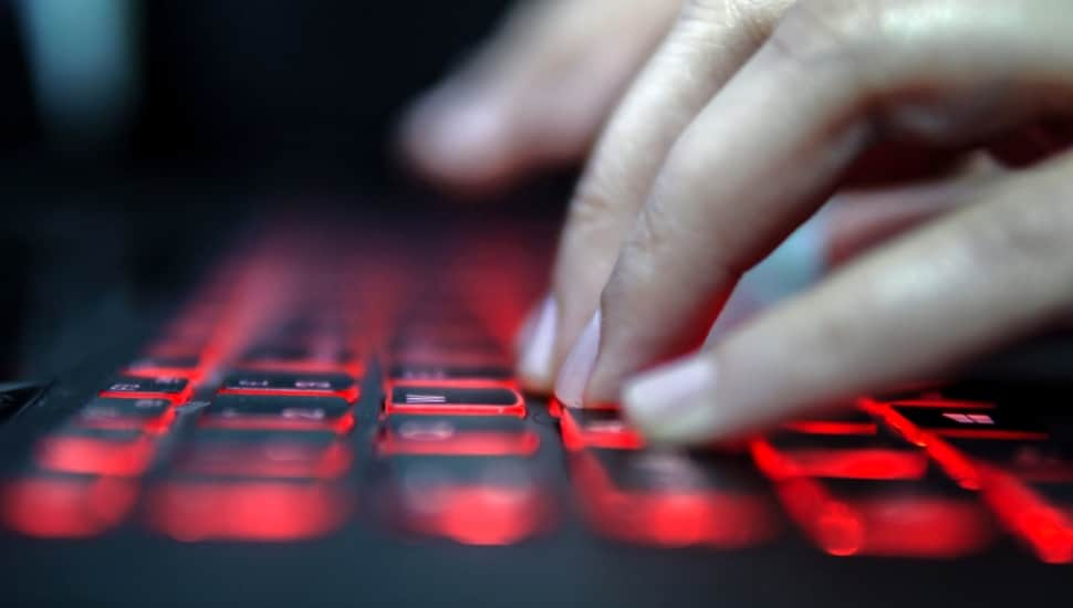 A hand types on a computer keyboard with the keys backlit in red.