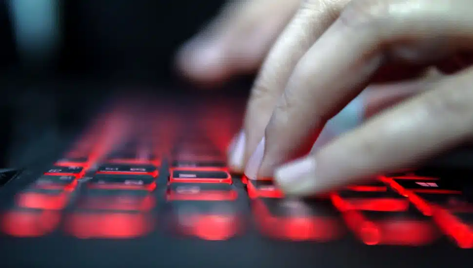 A hand types on a computer keyboard with the keys backlit in red.