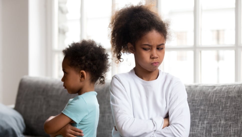 Two siblings, a young boy and girl, are facing away from each other angry.