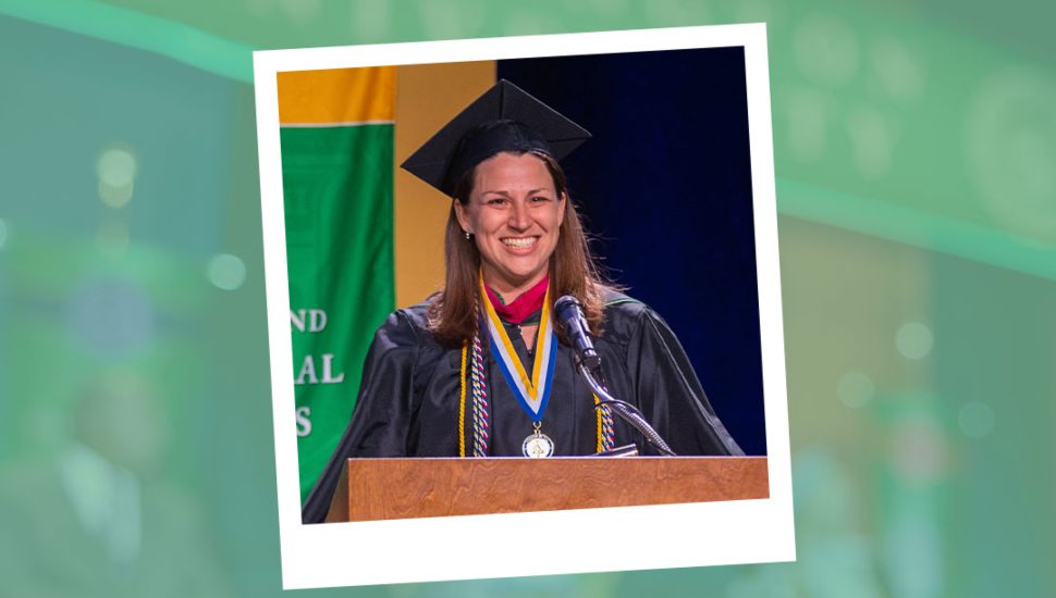 Abigail Hammer-Rupp delivers a speech at the podium during the 2025 Wilmington University College of Technology commencement ceremony, wearing graduation regalia and honors cords.