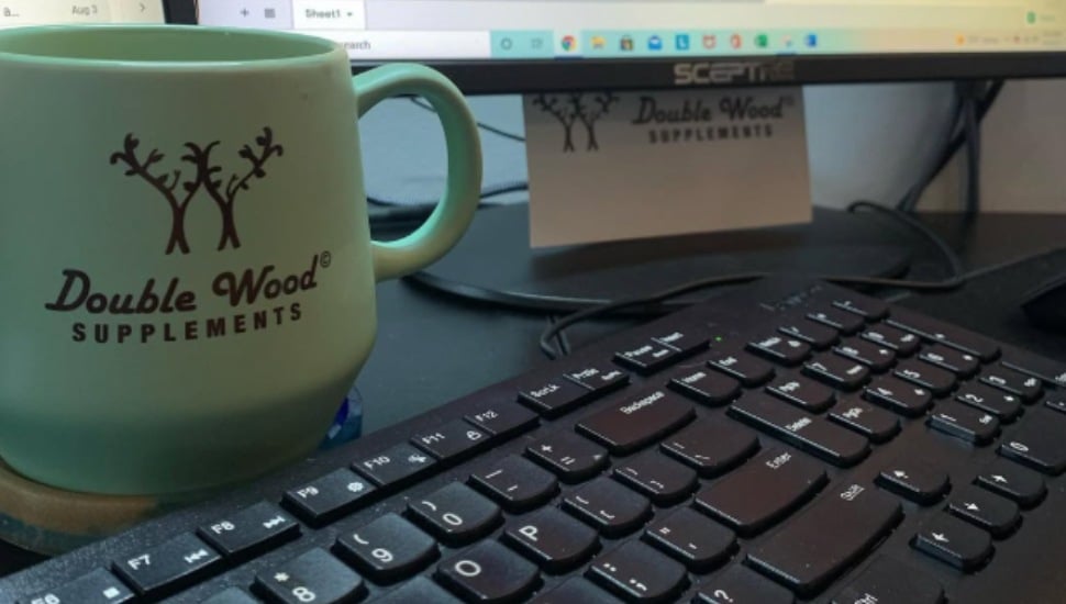 A Double Woods Supplement-branded coffee mug sits next to a keyboard.